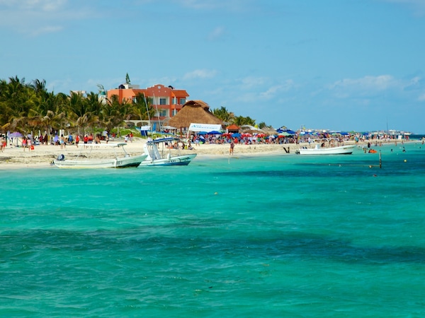 Belebter Strand mit türkisfarbenem Wasser und Booten.