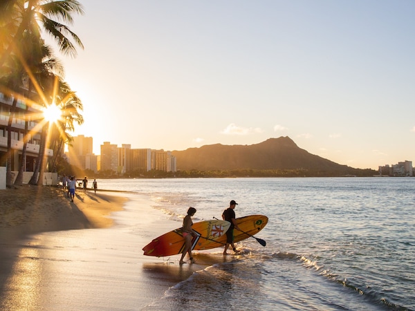 Strand mit Palmen und Surfern im Sonnenuntergang.