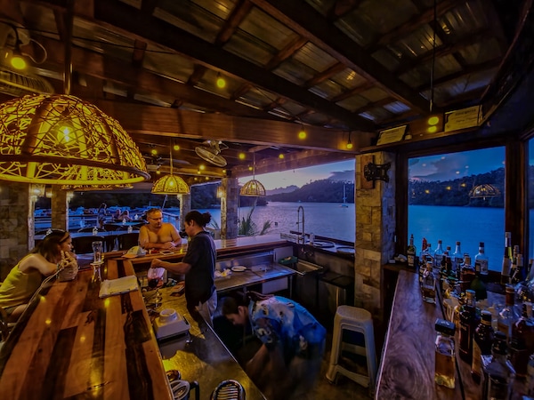 Bar mit Holzmöbeln und Hängelampen mit Blick auf See und Berge.