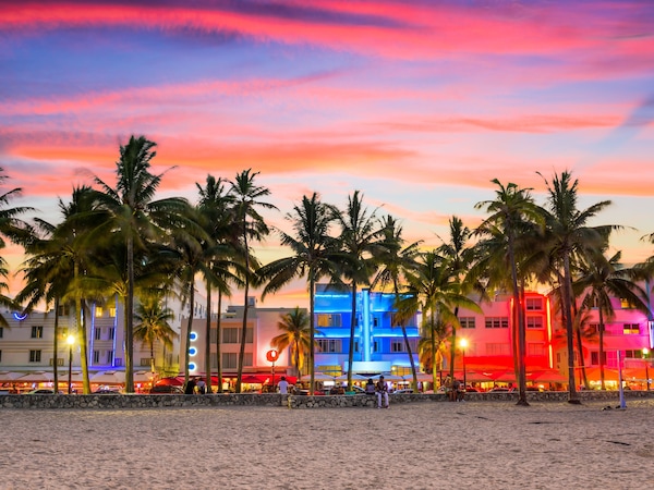 Strand mit Palmen und bunten Gebäuden im Sonnenuntergang.