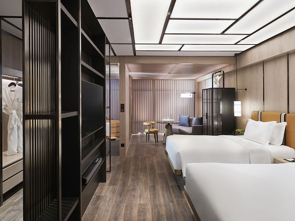 Hotelzimmer mit zwei Betten, begehbarem Kleiderschrank und einem kleinen Tisch mit Stühlen.