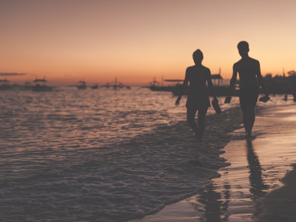 Silhouetten von Menschen am Strand im Sonnenuntergang, mit Booten im Hintergrund.