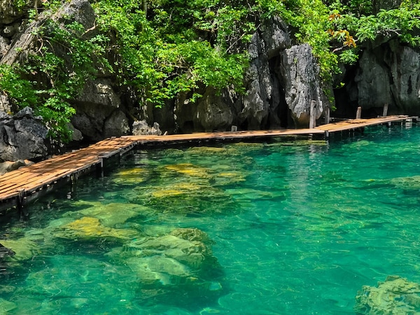 Holzsteg im klaren türkisfarbenen Wasser, umgeben von Felsklippen und üppigem Grün.